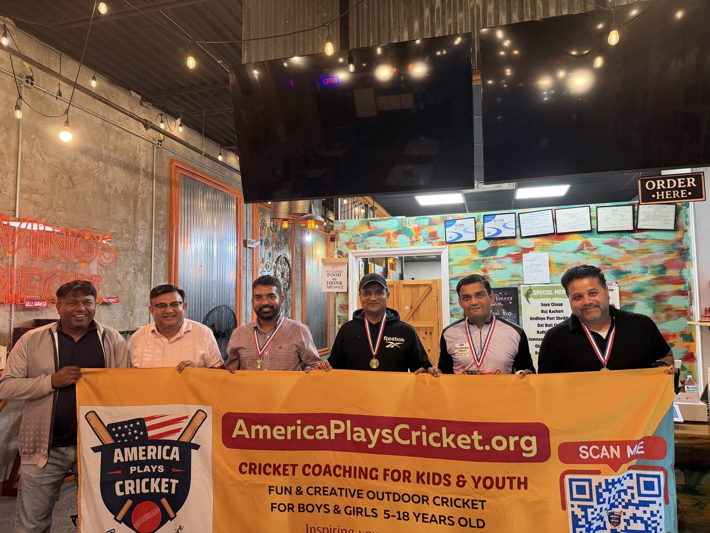 Coaches and organizers holding the America Plays Cricket banner